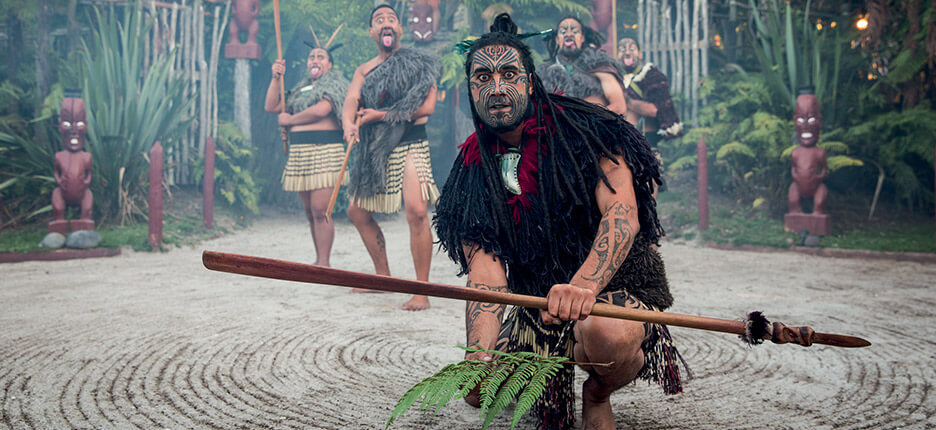 Image of a Maori Warrior with the haka in the background at Tamaki Maori village